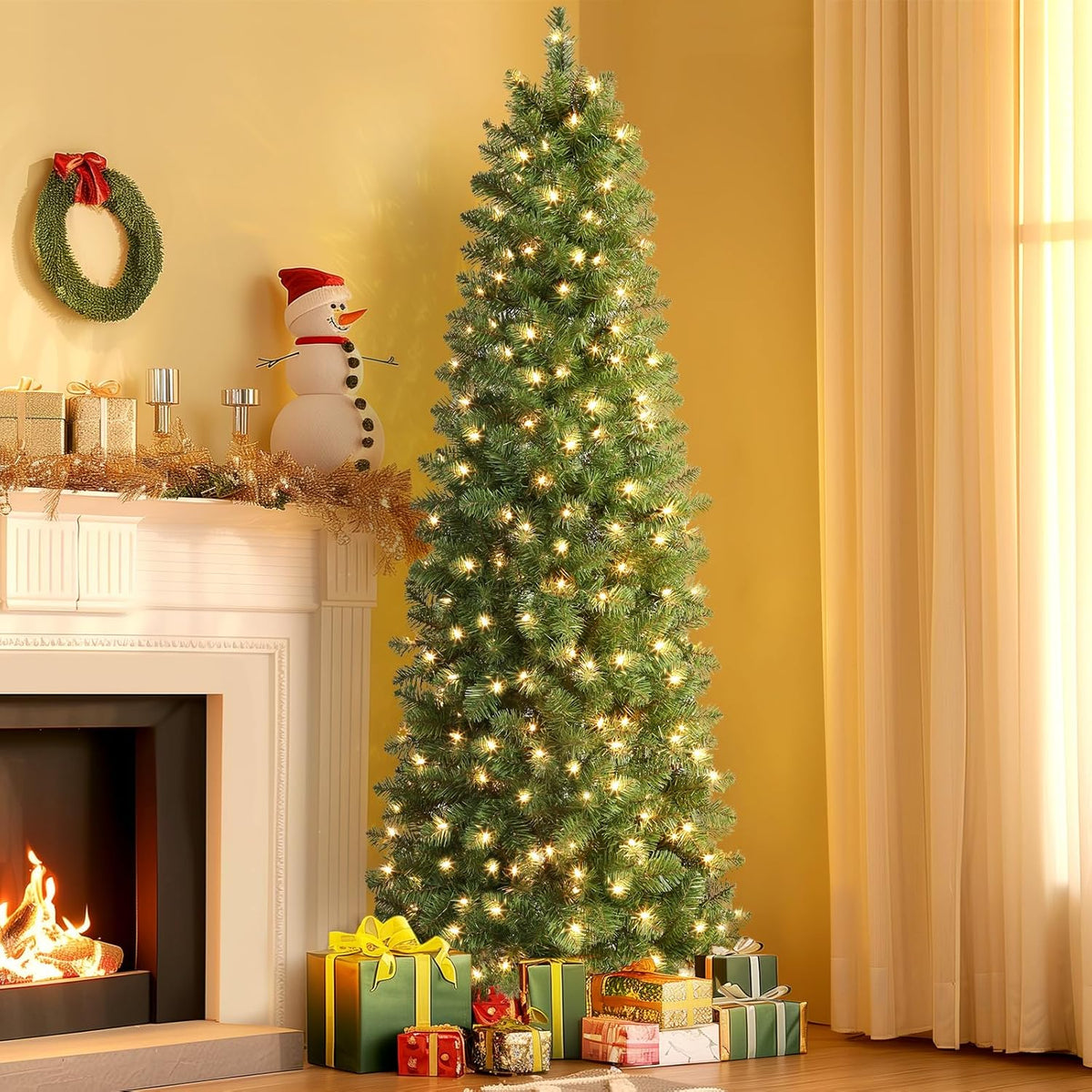 Green pencil Christmas tree with warm white lights beside a fireplace, curtains and wrapped gifts.