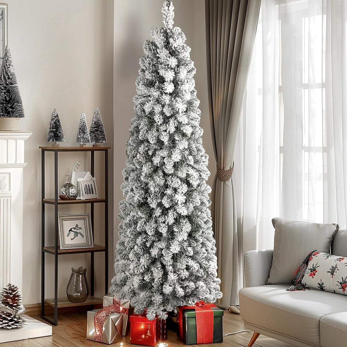 Snow-flocked pencil tree shown with its lights off beside a window and armchair.
