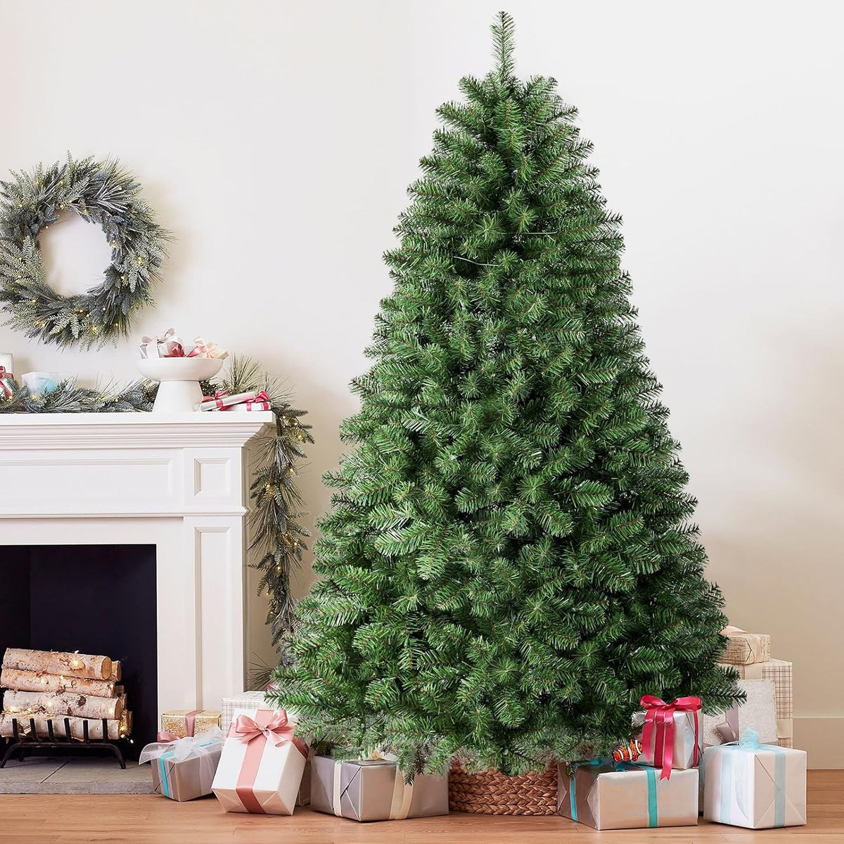 Green classic spruce tree shown with its lights off beside a fireplace and wrapped gifts.