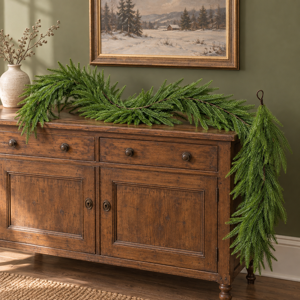 Nine-foot Norfolk pine garland styled along a wooden sideboard. AI-generated product styling image based on the original Amazon product image; accessories shown are styling props.